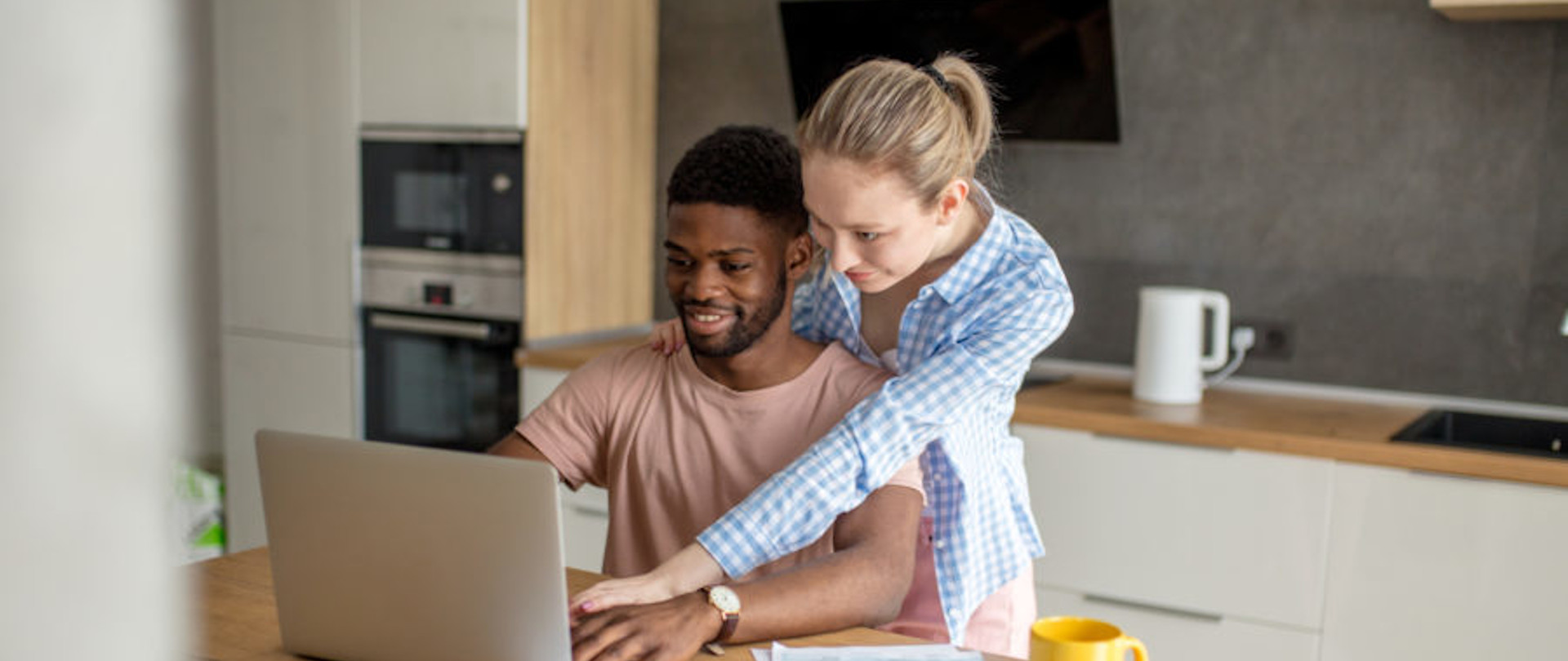 Young interracial couple using laptop together having breakfast at home Young interracial couple